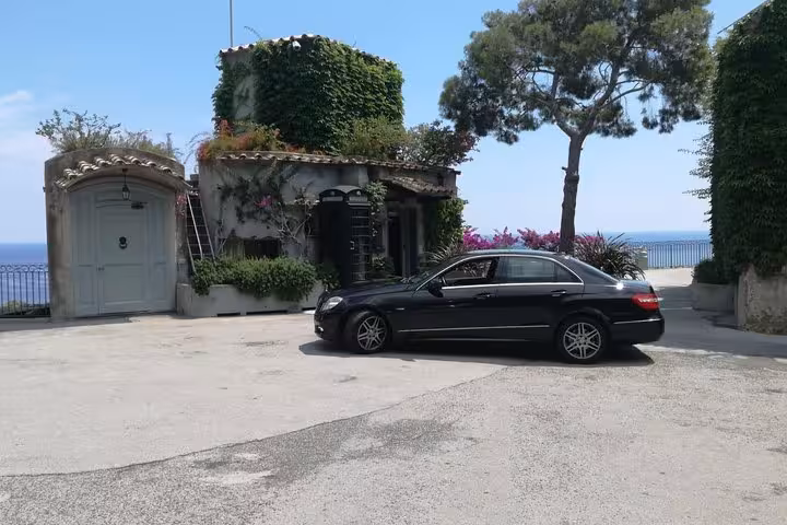 Luxury black car parked by a charming villa, offering private transfer from Naples to Sorrento with scenic views.
