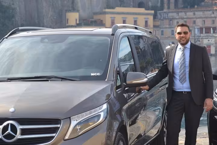 Professional driver with luxury van offering private transfer from Naples to Sorrento with scenic backdrop.