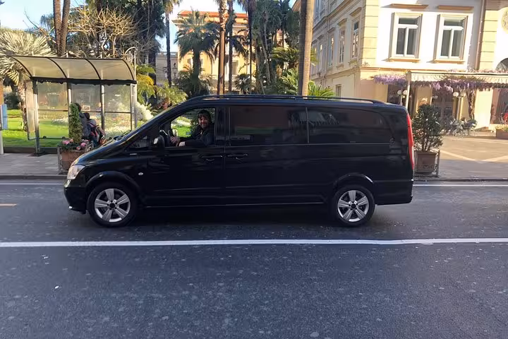 Luxury black van in sunny Sorrento street, offering private transfer service from Naples hotel, airport, or train station.