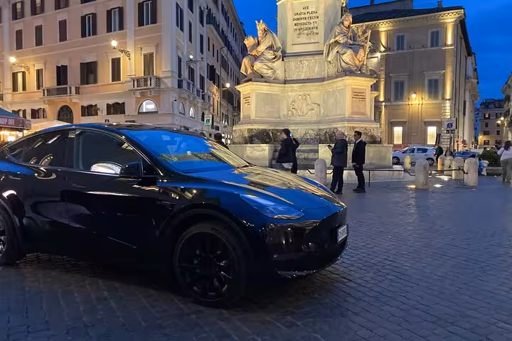 Elegant car in a bustling Roman square at night, ideal for private transfers to Fiumicino Airport.