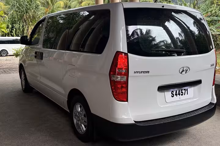 Spacious white Hyundai minivan ready for private transfers in Seychelles with lush tropical background.