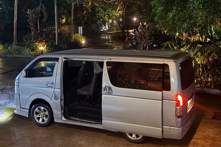 Silver minivan ready for private transfer service in Seychelles, parked at a lush tropical location at night.