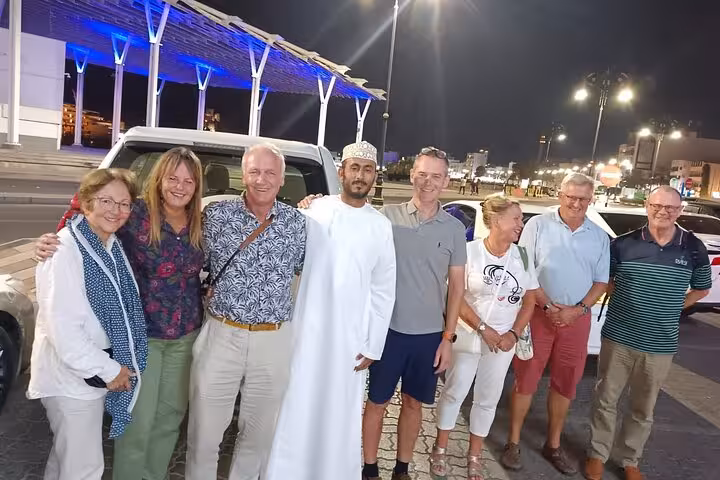 Happy small group with local driver standing by private car at night before transfer from Shangri-La to Muscat Airport