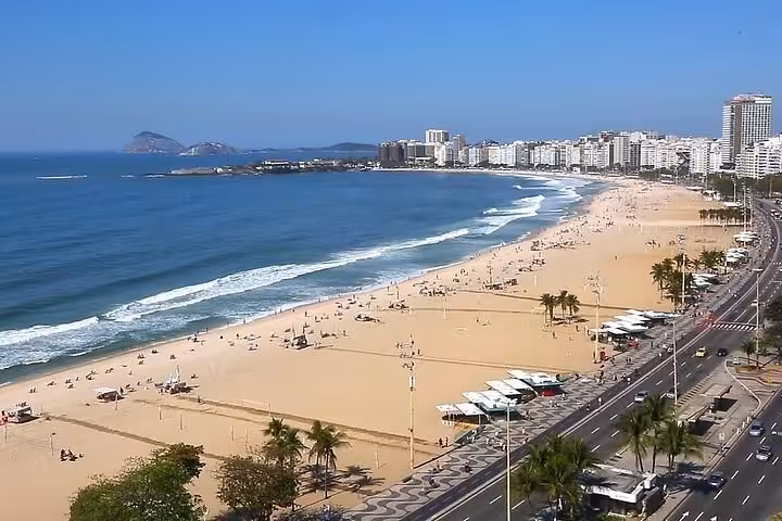 Scenic view of Copacabana Beach with blue sky, perfect for private transport from Búzios to Rio de Janeiro tours.
