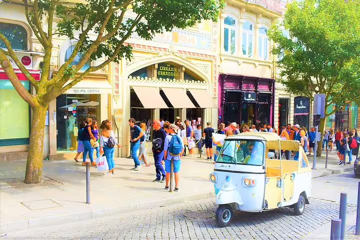 A vintage tuk tuk is parked on a bustling cobblestone street in the historic city center, surrounded by tourists and colorful buildings.