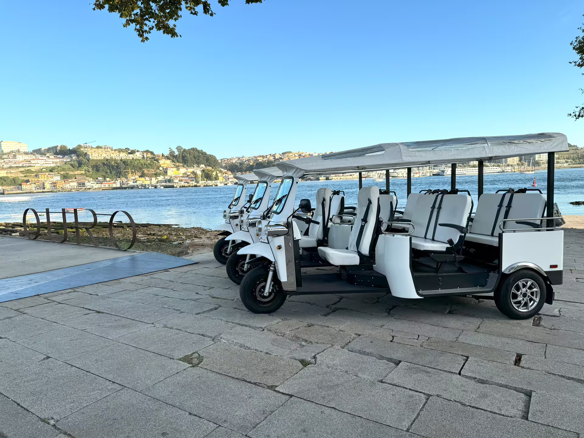 White tuk tuks parked by the scenic riverside, ready for a private tour of the historic city center on a cruise shore excursion.