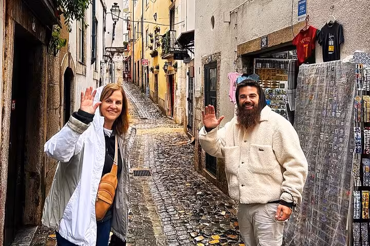 Guests waving in a narrow Alfama street during a 4-hour private tuk tuk tour in Lisbon with local guide