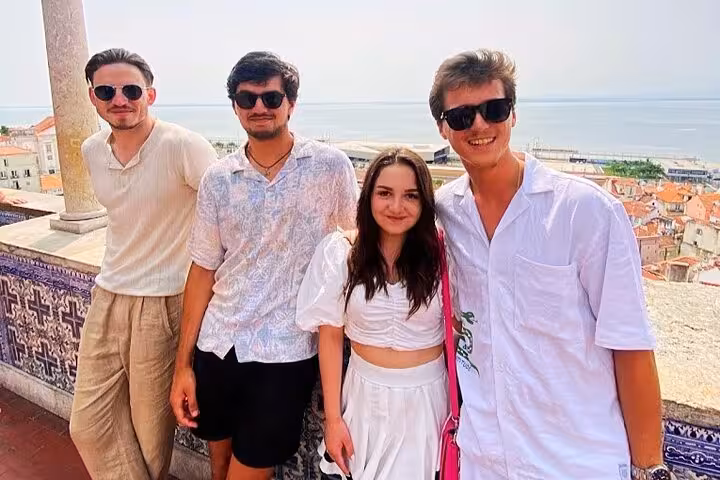 Friends enjoying Lisbon viewpoint stop on a 4-hour private tuk tuk tour, with Alfama rooftops behind