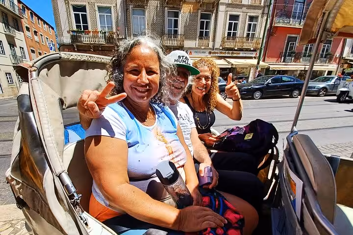 Happy travelers riding a private tuk tuk tour in Lisbon through historic streets and colorful buildings