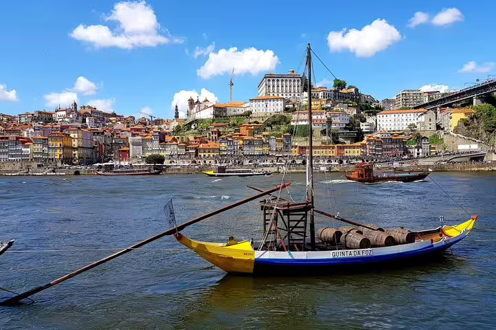 Traditional Rabelo boat on Douro River with Porto's historic center backdrop, perfect for a private tuk tuk shore excursion.