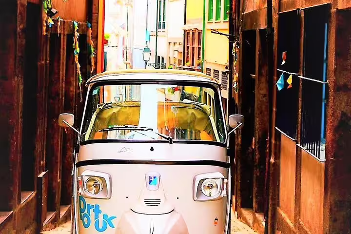 Charming TukTuk navigating narrow, colorful streets of Porto on a private half-day tour showcasing the city's vibrant architecture.
