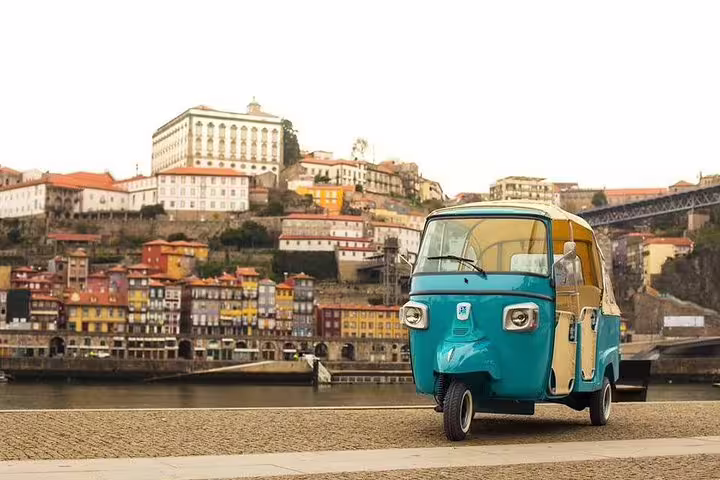 Vibrant turquoise tuk-tuk parked along Porto's scenic riverside, offering a unique half-day private tour of the city's historic sites.