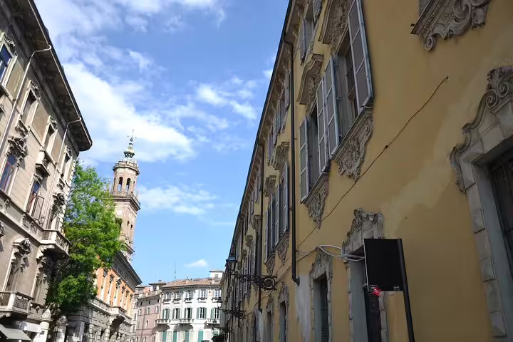 Elegant pastel palazzi and bell tower lining a sunlit cobbled street explored on a private walking tour of Parma