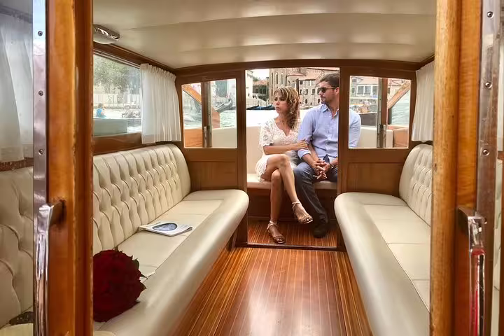 Elegant couple enjoying a private water taxi ride from Santa Lucia station to Venice city center hotel.