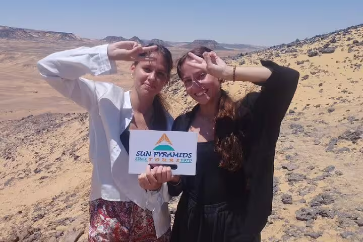 Two travelers hold tour sign on a desert ridge near Bahariya Oasis, part of a private 4-day White Desert trip