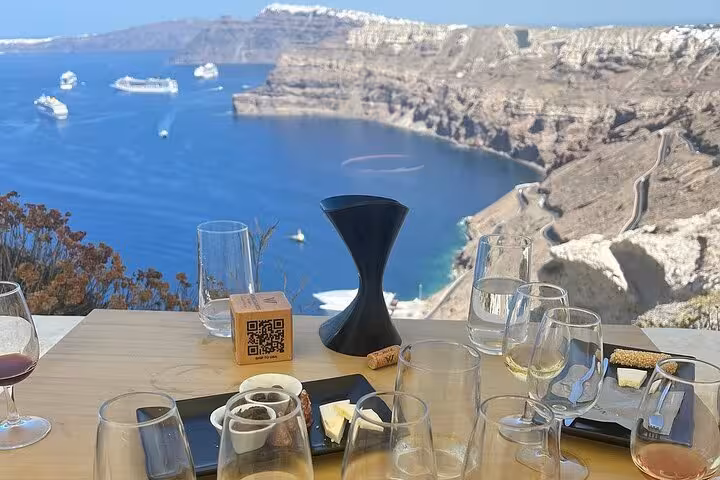 Wine tasting table with glasses and snacks overlooking Santorini caldera, part of private winery tour and Wine Museum