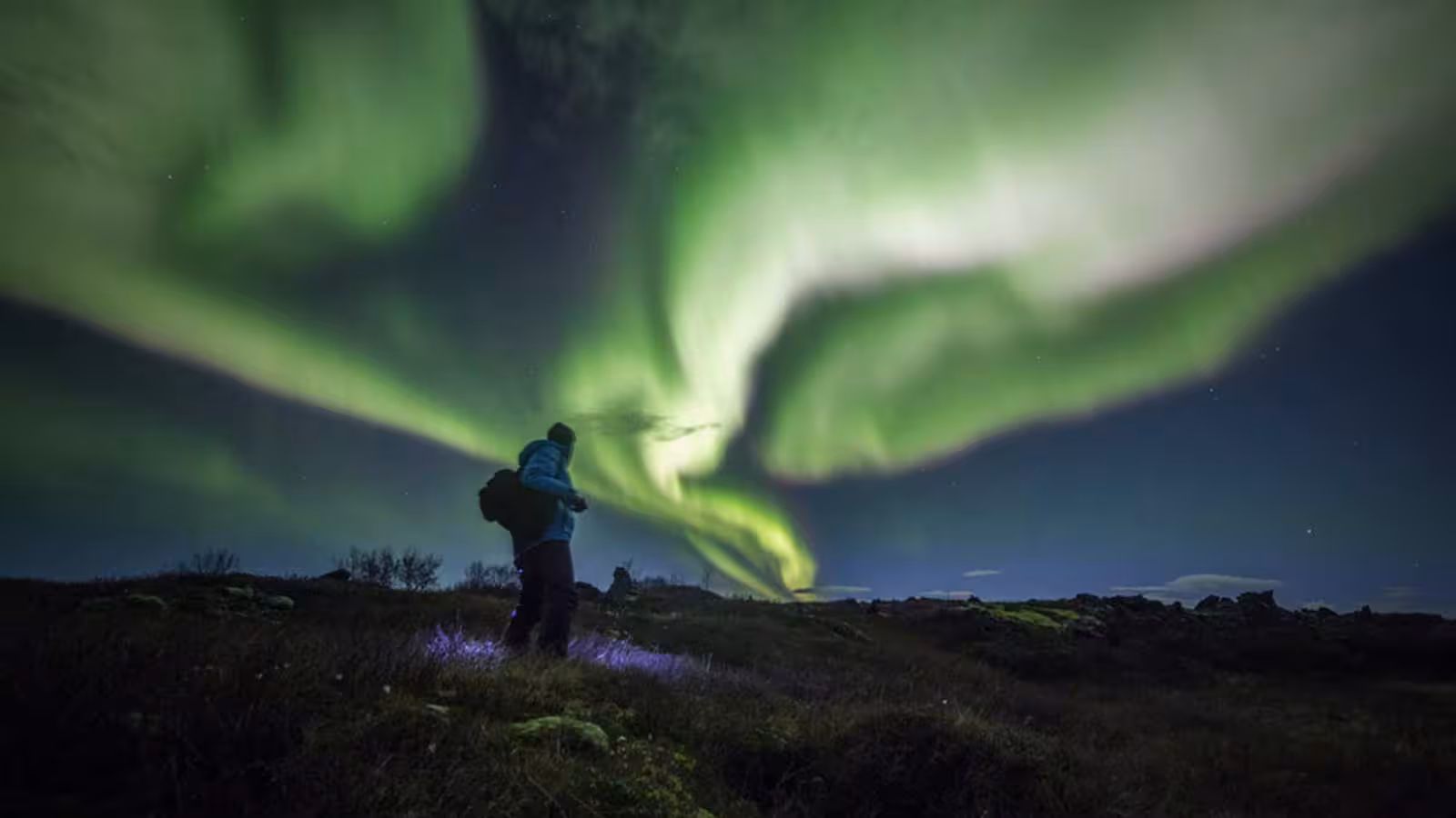 Traveler enjoying vibrant Northern Lights display during Private Winter Golden Circle Tour in Iceland.