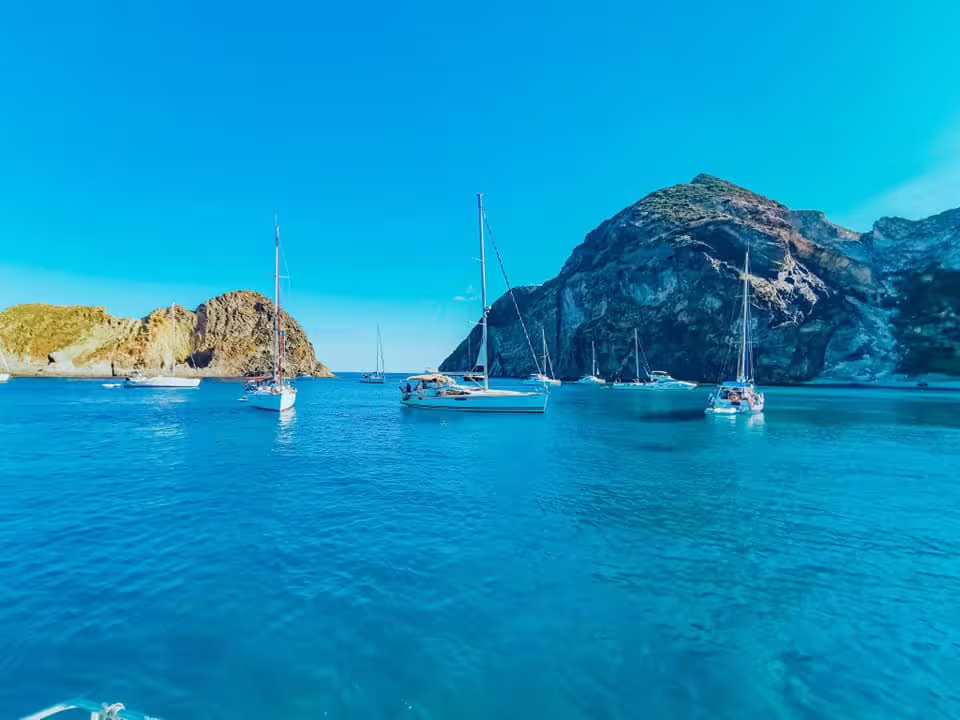 Yachts anchored in turquoise bay against rocky Procida coastline on a relaxing full-day boat tour from Ischia