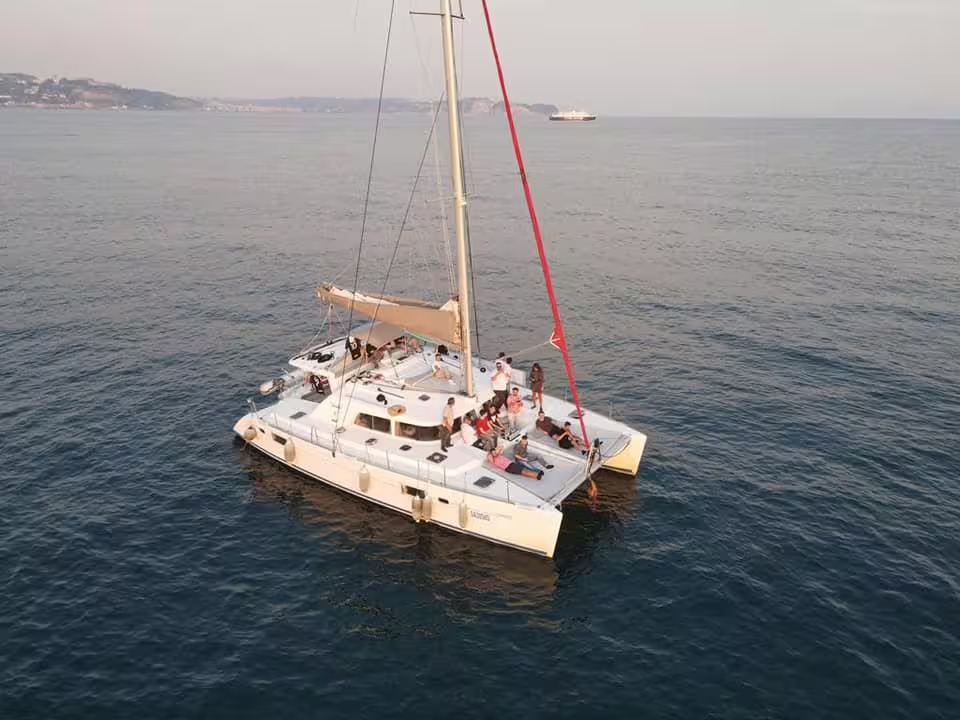 Group enjoying a relaxing Procida by catamaran tour on calm Tyrrhenian Sea waters, with coastal views in the distance