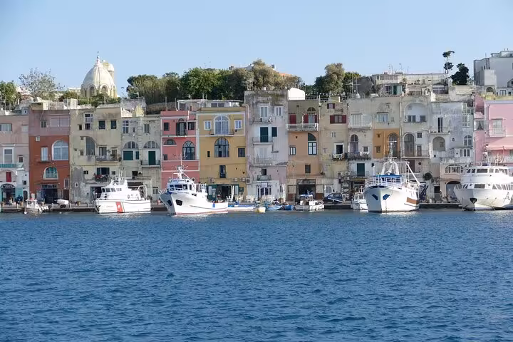 Picturesque waterfront of Procida with pastel-colored buildings and anchored boats, ideal for a Naples day trip.