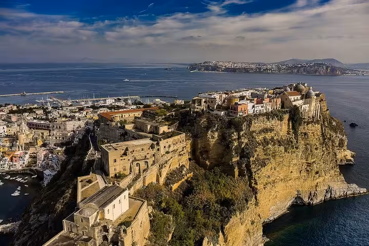 Aerial view of Procida Island's historic architecture perched on cliffs overlooking the serene blue waters, perfect for a boat tour.