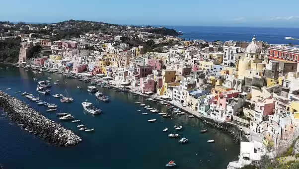 Aerial view of Procida’s pastel harbor lined with fishing boats and domed church, visited on a full day VIP catamaran cruise