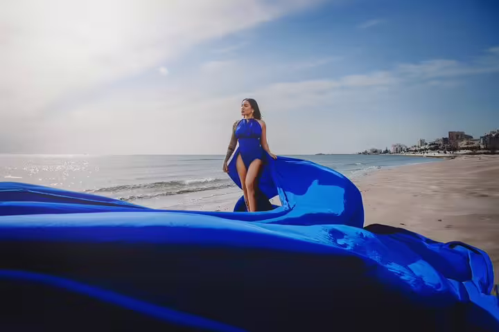Elegant woman in a flowing blue dress poses on a serene Ayia Napa beach during a professional photoshoot.