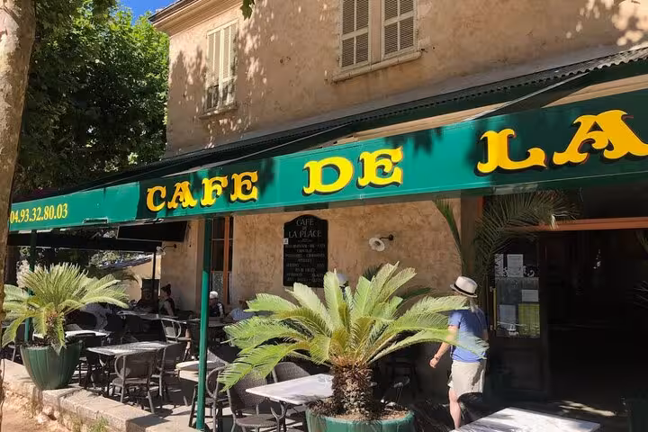 Quaint Café de la Place with vibrant green awning in a scenic village, ideal for a Provencal countryside tour.