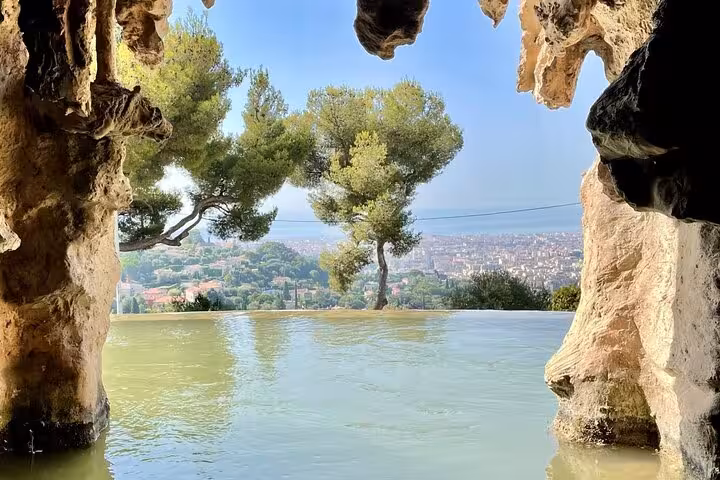 Scenic view through a rocky cave opening overlooking a serene landscape with trees and a distant city.