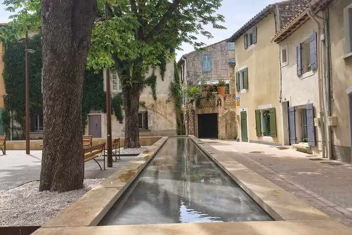 Charming street in Provence with a tranquil canal and rustic stone houses, perfect for a leisurely stroll.