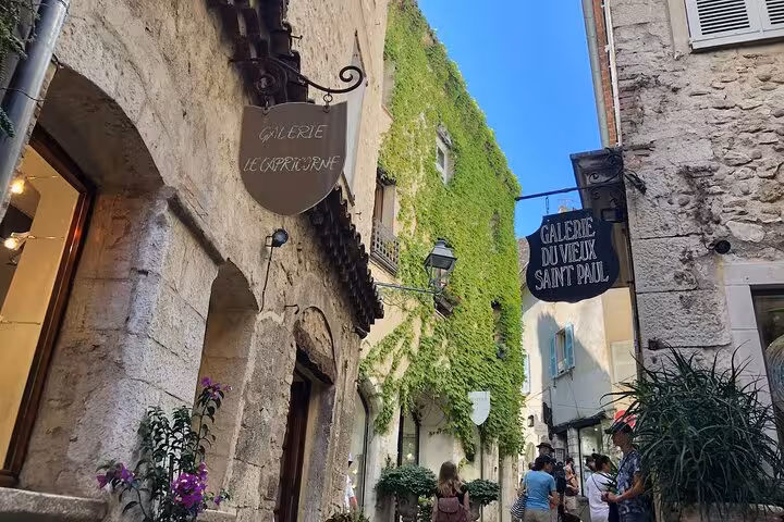 Charming cobblestone street in a Provence village, lined with art galleries and lush greenery under a clear blue sky.