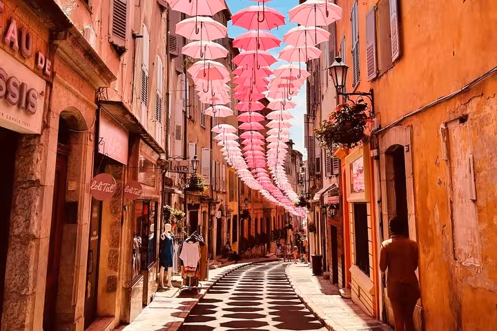 Vibrant street in Provence adorned with pink umbrellas creating a whimsical atmosphere in a quaint village setting.
