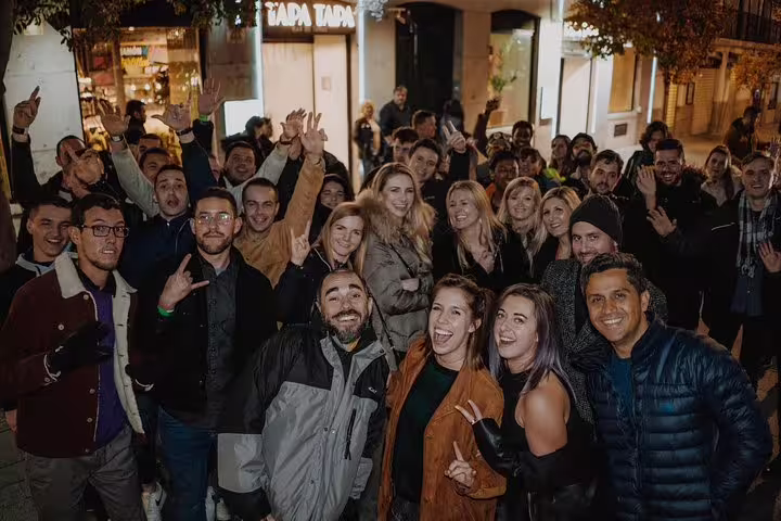 Large group of excited people gathering outside a tapas bar on a Madrid pub crawl tour, highlighting nightlife fun.