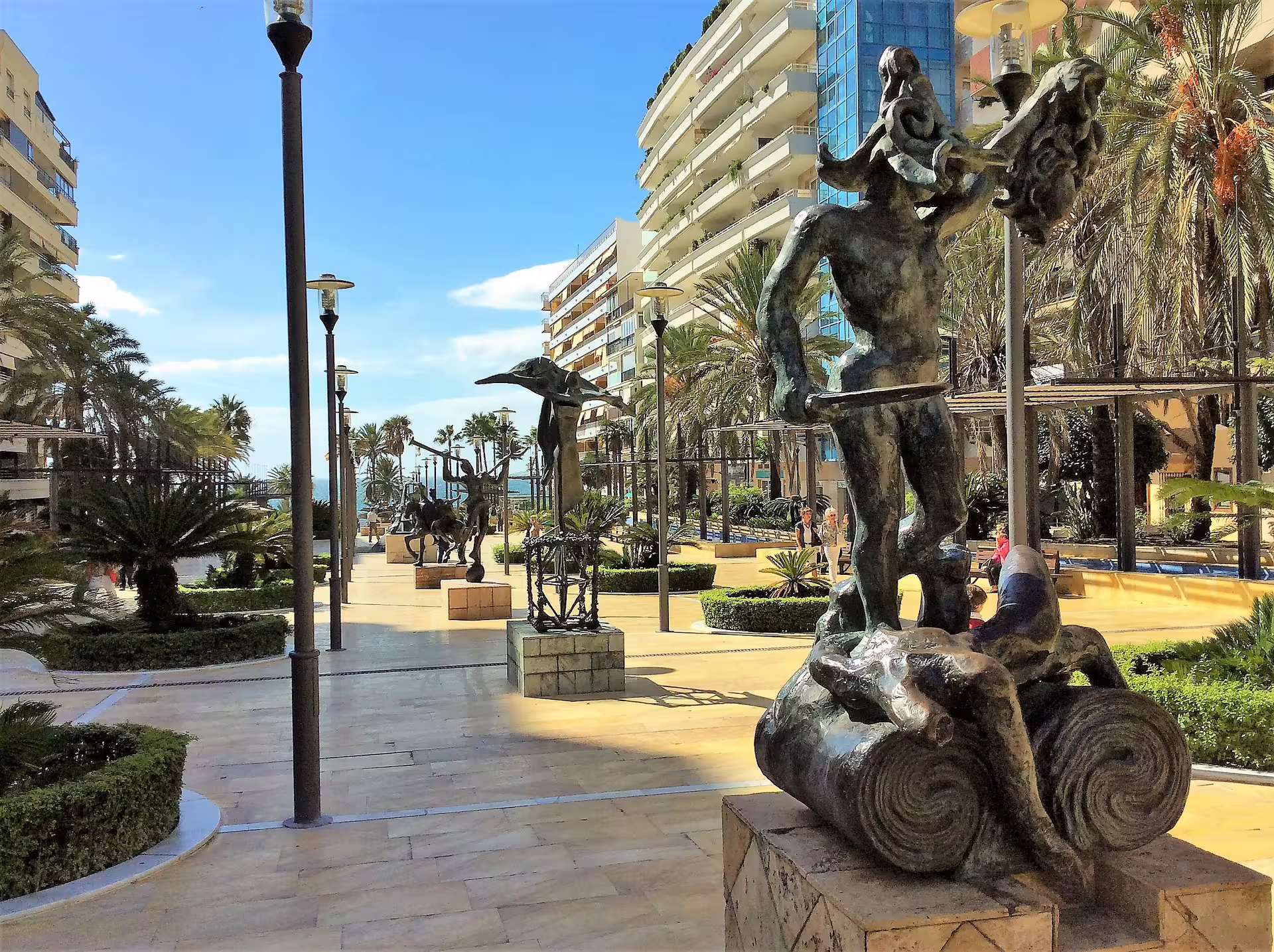 Puerto Banus promenade sculptures and palm-lined walkway in Marbella, seen on Costa del Sol group tour pick-up