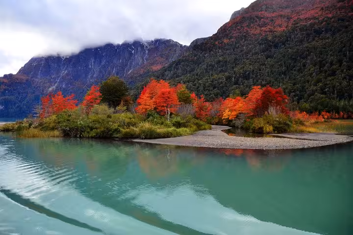 Vibrant autumn foliage reflecting in the turquoise waters of Lake Frías with majestic mountains in the background.
