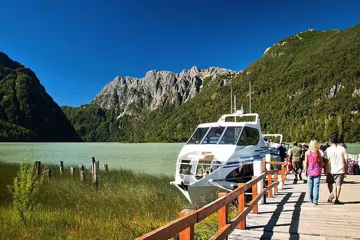Scenic view of a boat docked at Lake Frías surrounded by lush green mountains and a wooden boardwalk in Puerto Blest.