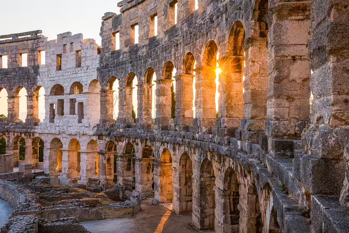 Golden sunset shining through Pula Arena arches, Roman amphitheater in Pula Croatia, admission ticket sightseeing