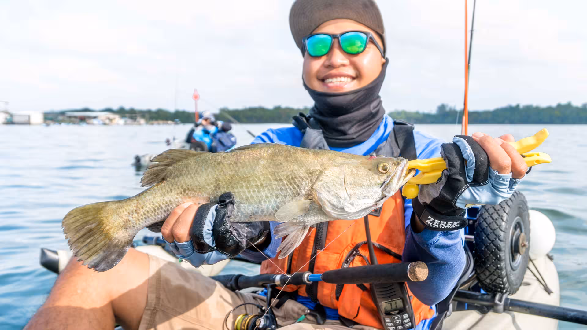 Smiling angler in a kayak holds a large fish caught during Pulau Ubin mangrove fishing adventure.