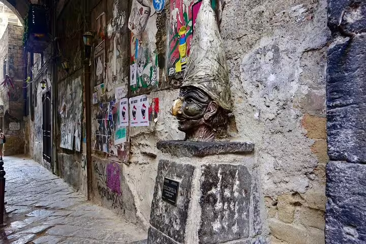 Pulcinella statue in a narrow graffiti-lined alley on Via dei Tribunali, Naples, featured on a legends and superstitions walking tour