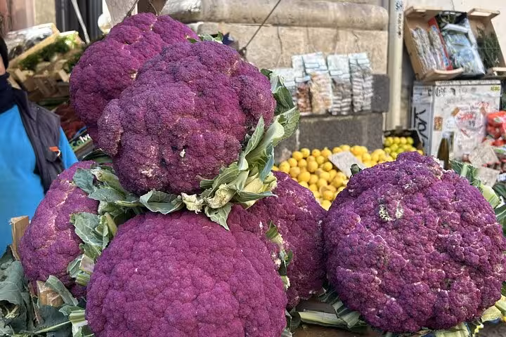 Vibrant purple cauliflowers on display at a bustling Catania street market, highlighting local produce and culture.