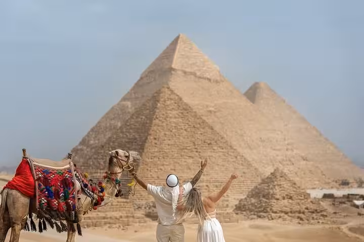 Tourists celebrate beside a decorated camel with the Pyramids of Giza on a full-day Cairo pickup tour
