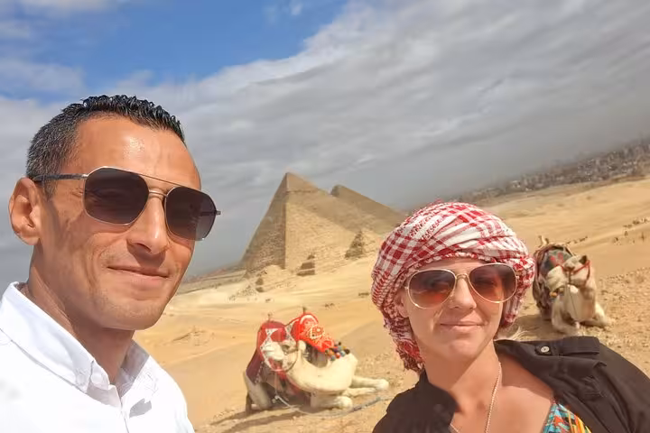 Tourists enjoying a sunny day with camels in front of the iconic Pyramids of Giza during a private Cairo tour.