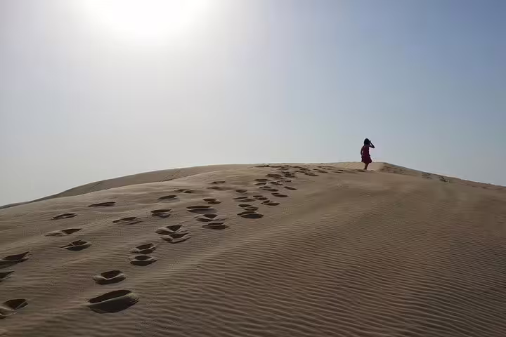 Lone traveler walks atop a sunlit sand dune, leaving footprints on Qatar's vast desert landscape.