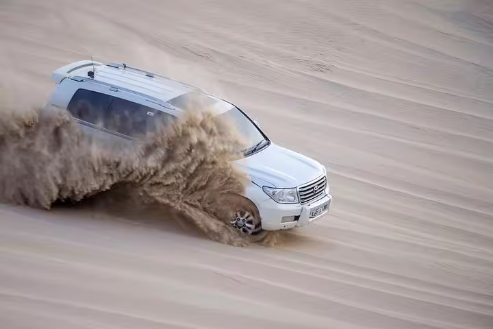 4x4 vehicle kicks up sand during an exhilarating dune bashing adventure in Qatar's desert landscape.