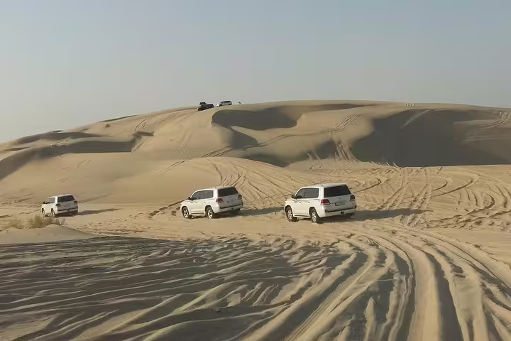 4x4 vehicles navigate towering sand dunes on a Qatar Gold Dune Safari, showcasing thrilling dune bashing adventure.