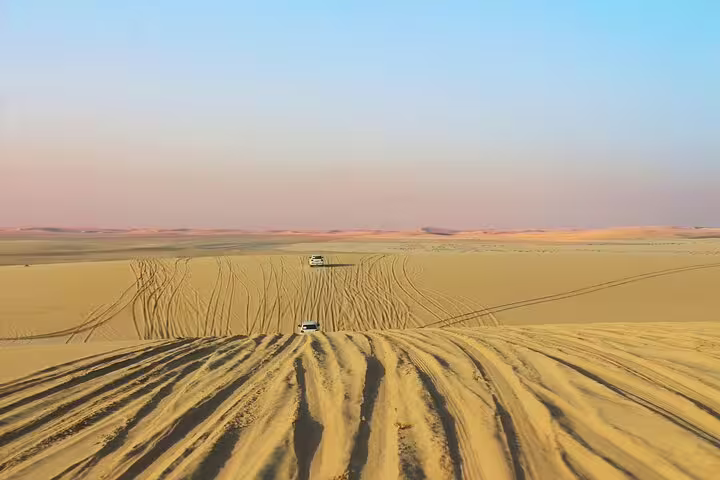 Off-road vehicles navigating the vast golden dunes of Qatar's desert under a clear sky, ideal for thrilling dune bashing.