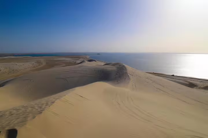 Golden sand dunes meet the tranquil waters of Qatar's Inland Sea, offering stunning vistas on a desert safari tour.