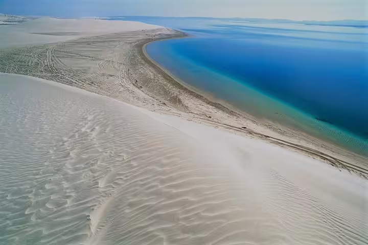 Aerial view of Qatar's Inland Sea Desert with golden dunes meeting crystal-clear blue waters for a serene landscape.