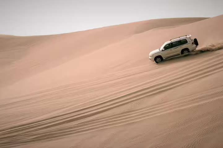 SUV performs thrilling dune bashing on the expansive sands of Qatar's Inland Sea Desert.