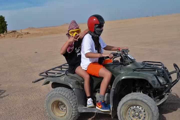 Two riders on an ATV quad in Sharm El Sheikh desert wearing helmets and goggles on a sunrise or sunset safari